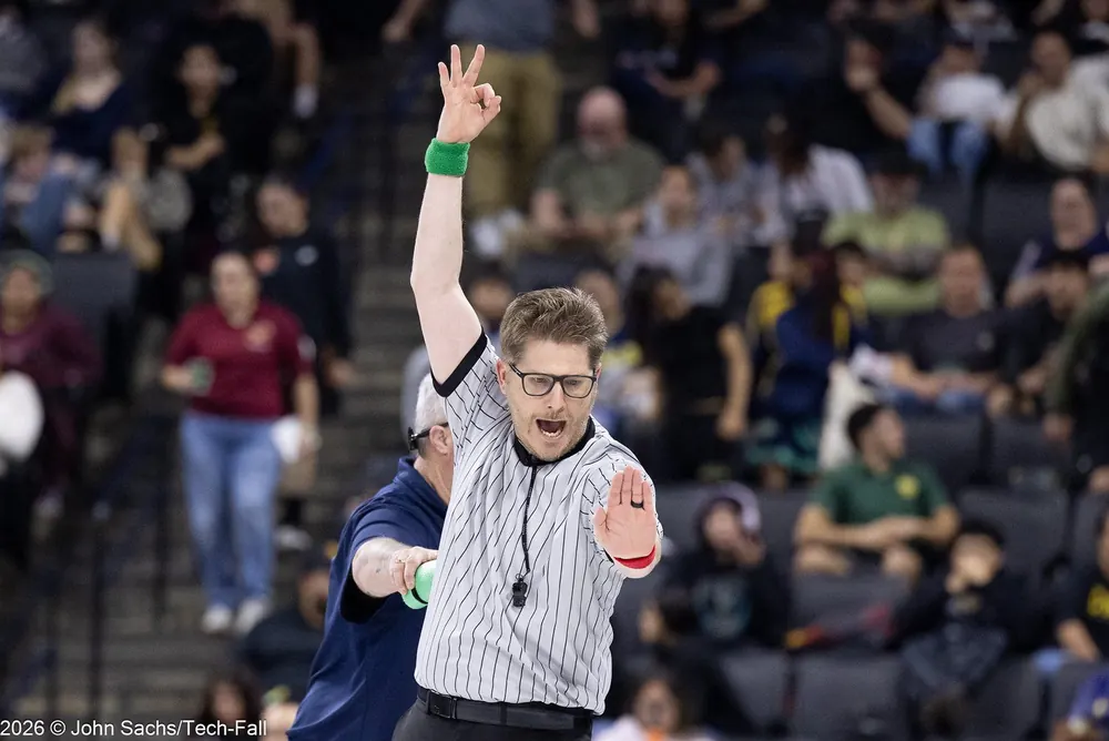 An official signals from the edge of the mat in a packed arena.