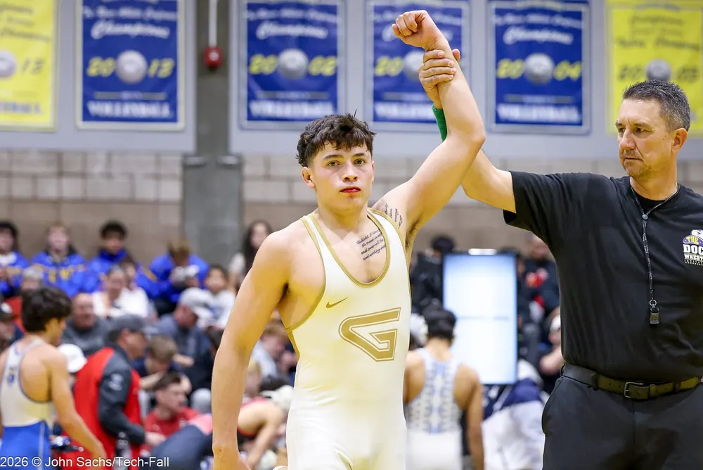 An official raises a wrestler's hand in a gym.