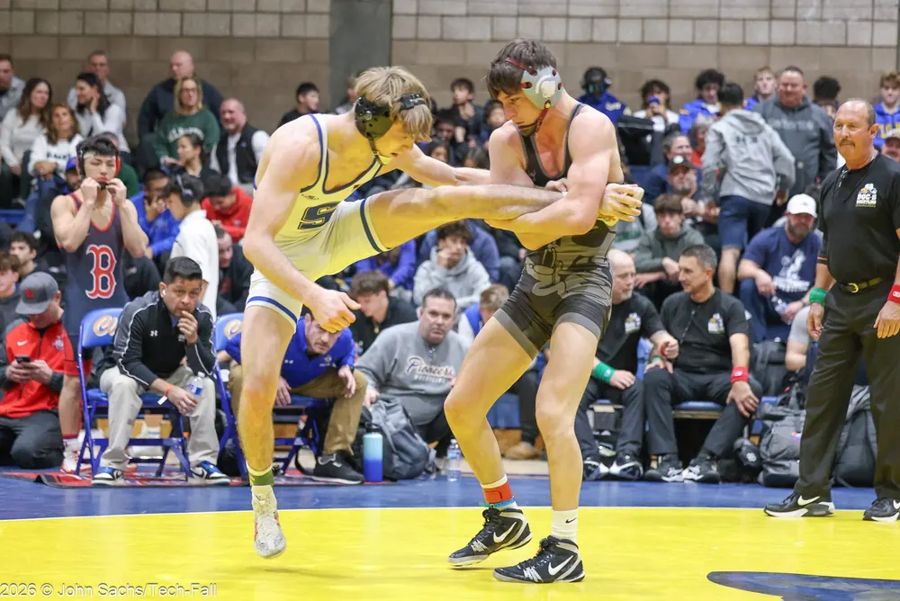 A match underway in a crowded gym, with an official at the edge of the mat.