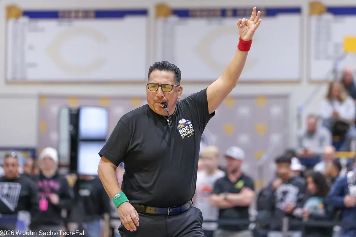 An official in a black polo signals two points during a match.